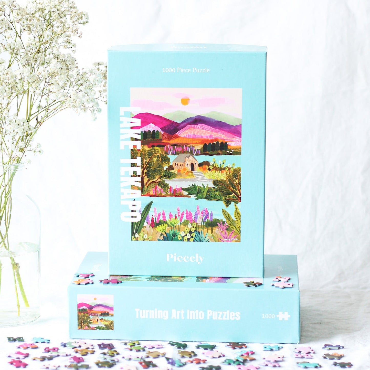 Nachhaltiges Puzzle mit 1000 Teilen, das den Lake Tekapo mit einem Häuschen, den Bergen im Hintergrund und vielen Pflanzen und Blumen zeigt.