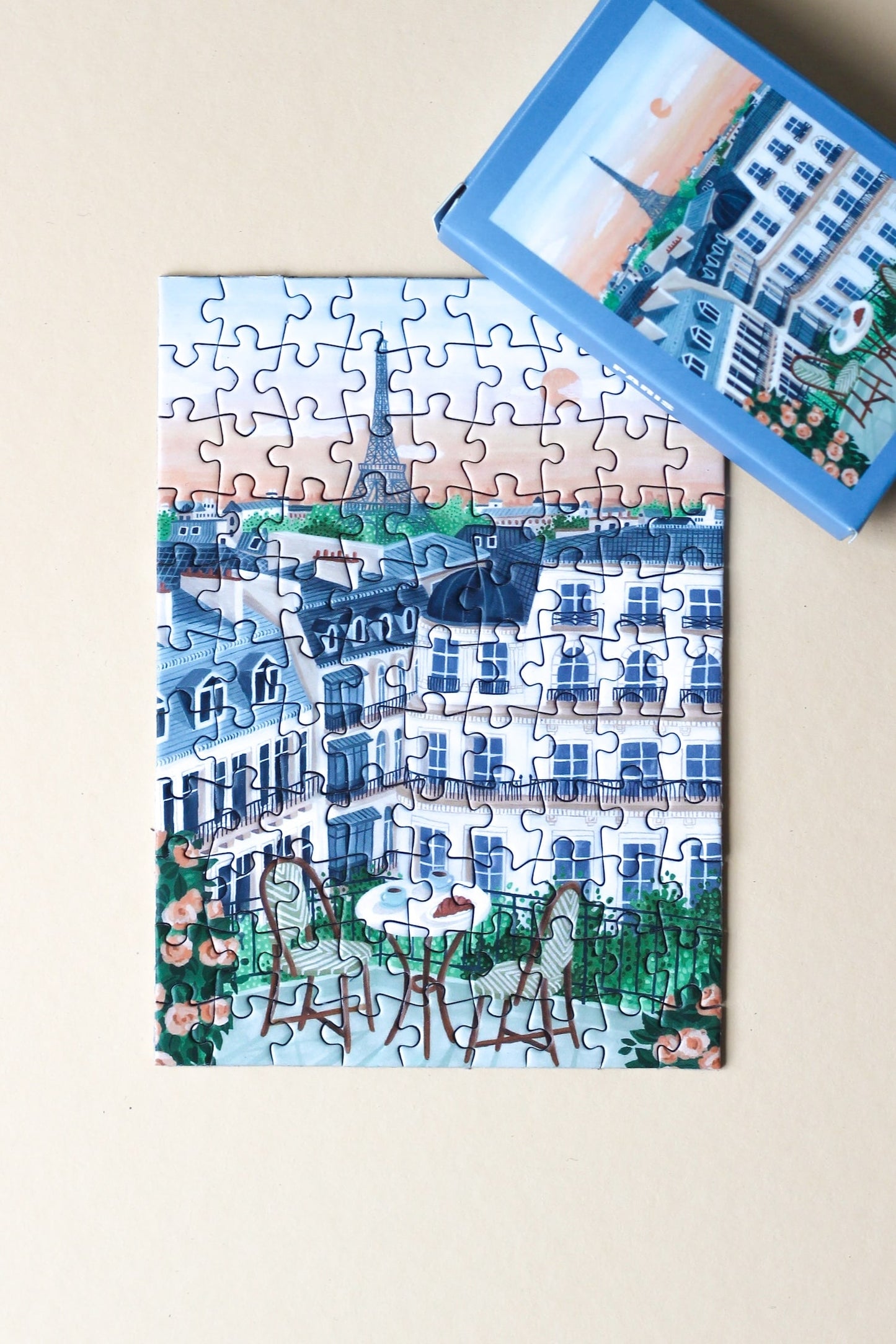 99-Teile-Mini-Puzzle „Paris“ von Piecely – Illustration eines Pariser Balkons mit Frühstückstisch, Rosen und Blick auf den Eiffelturm, auf hellblauer Verpackung.