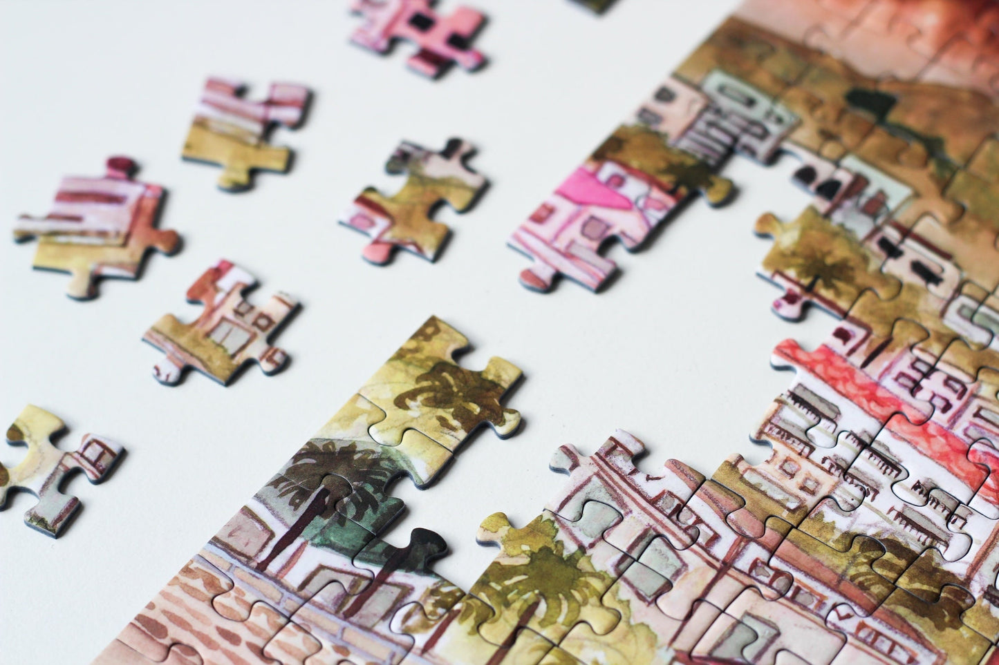 500-teiliges Puzzle für Erwachsene, das die Strandpromenade des Kapstädter Viertels Camps Bay zeigt. Im Vordergrund sind man Sandstrand und blaues Meer und im Hintergrund Häuserketten und die Berge.