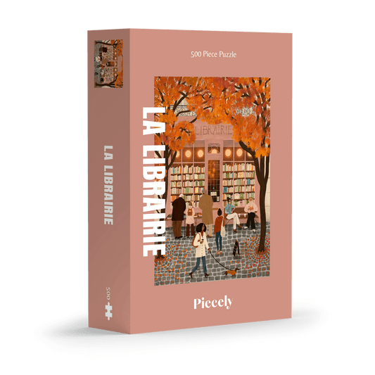 500-Teile-Puzzle „La Librairie“ von Piecely – Illustration einer herbstlichen Pariser Straßenszene vor einer kleinen Buchhandlung, auf rosa-brauner Verpackung.