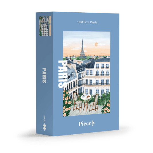 1000-Teile-Puzzle „Paris“ von Piecely – Illustration eines Pariser Balkons mit Frühstückstisch und Blick auf den Eiffelturm, auf hellblauer Verpackung.