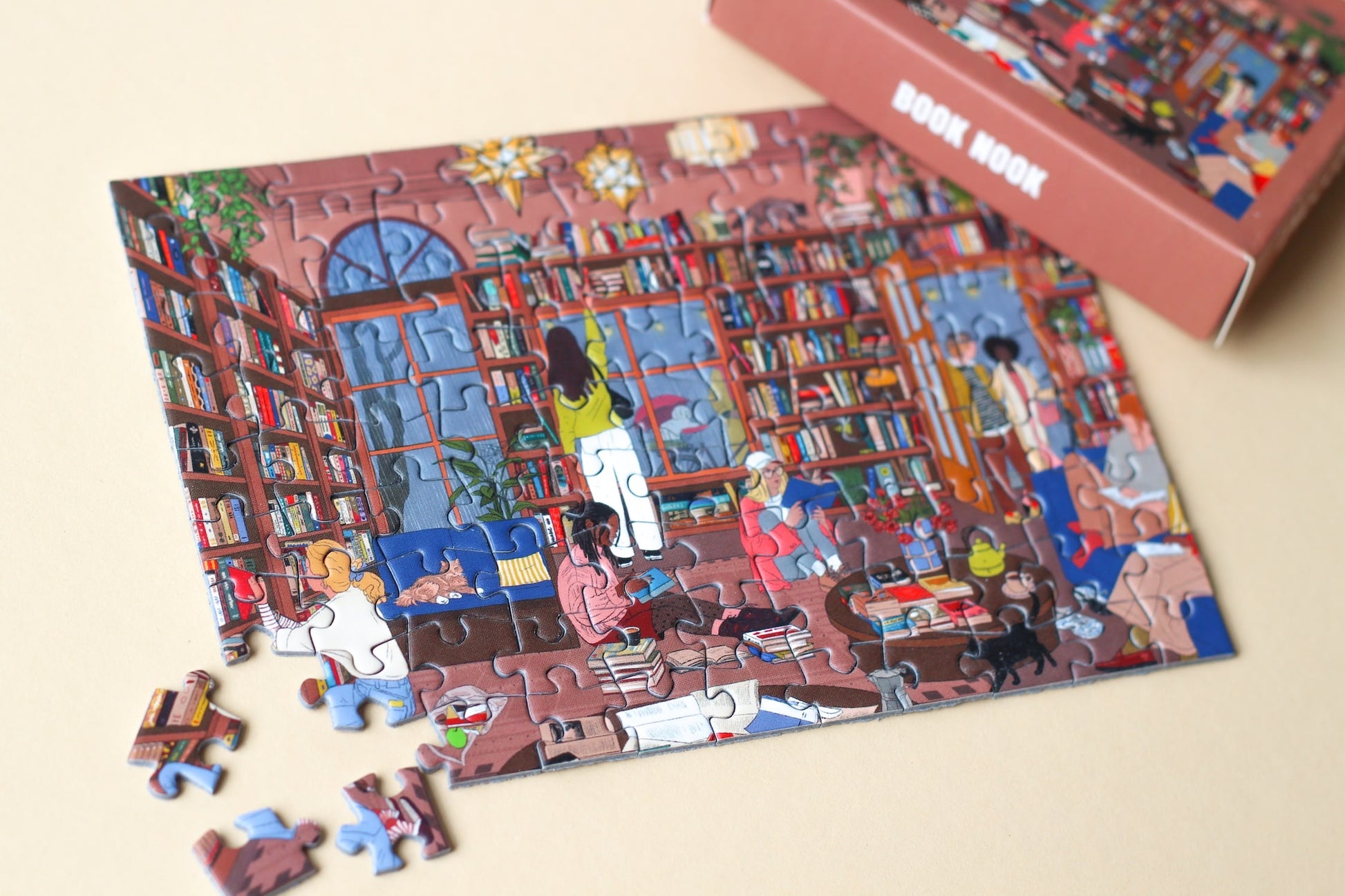 99-Teile-Mini-Puzzle „Book Nook“ von Piecely – Illustration eines gemütlichen Leseraums mit Bücherregalen und Menschen beim Lesen, auf brauner Verpackung.