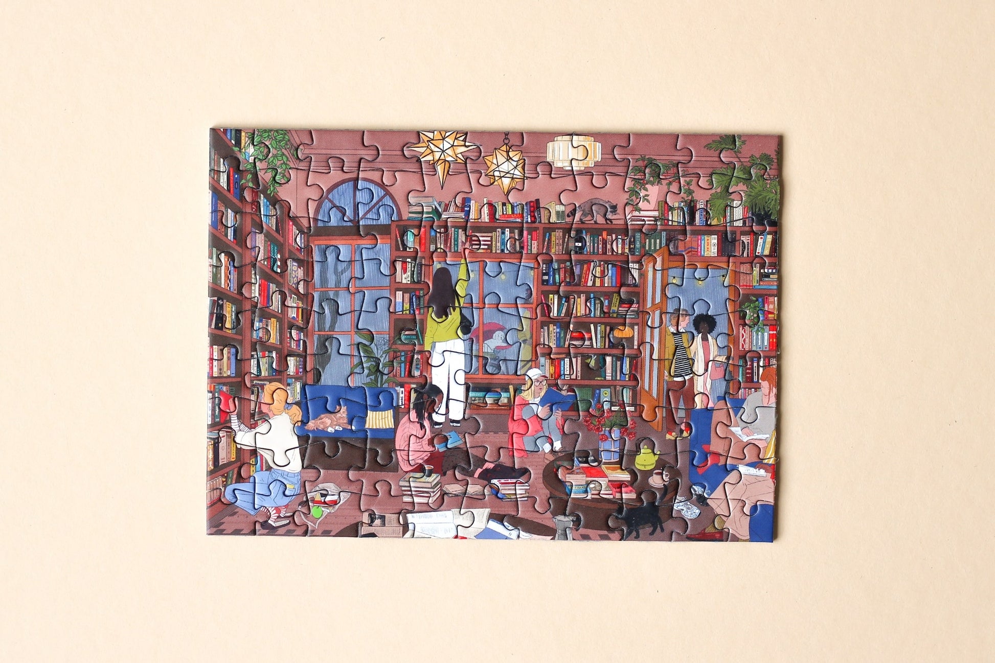 99-Teile-Mini-Puzzle „Book Nook“ von Piecely – Illustration eines gemütlichen Leseraums mit Bücherregalen und Menschen beim Lesen, auf brauner Verpackung.