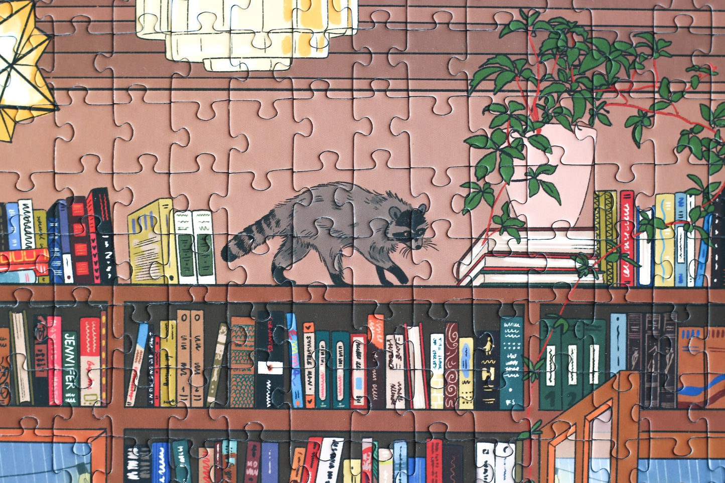1000-Teile-Puzzle „Book Nook“ von Piecely – Illustration einer gemütlichen Bibliothek mit Bücherregalen, Lesenden und warmem Licht, auf brauner Verpackung.
