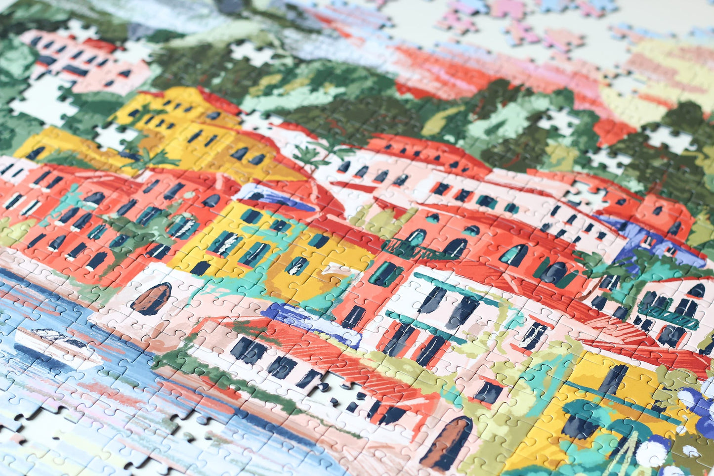 1000-teiliges Puzzle für Erwachsene, das den Comer See in Varenna zeigt. In der Bucht befinden sich zwei Boote und die Sicht auf den See ist gesäumt von bunten Häusern.