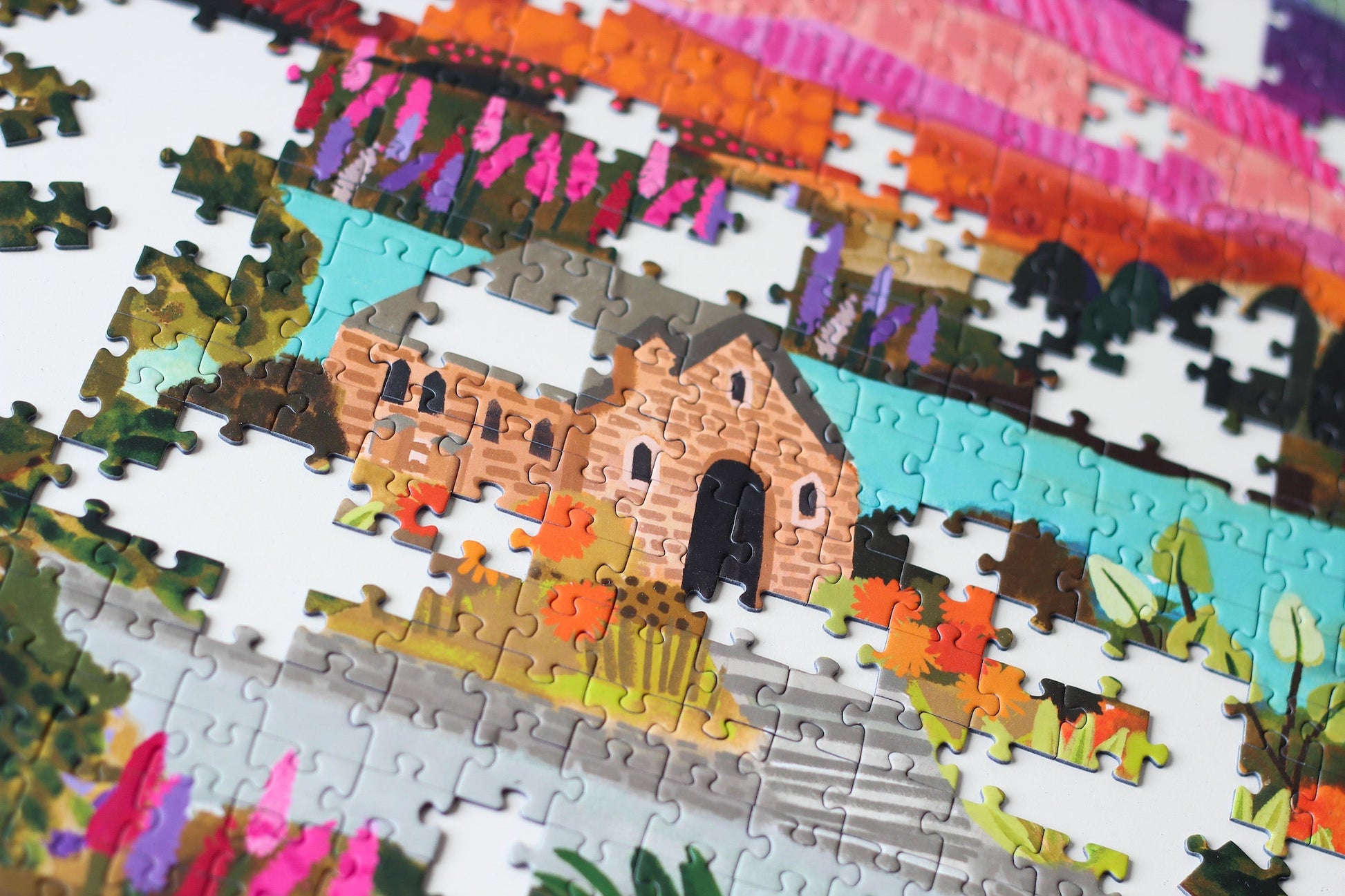 Nachhaltiges Puzzle mit 1000 Teilen, das den Lake Tekapo mit einem Häuschen, den Bergen im Hintergrund und vielen Pflanzen und Blumen zeigt.