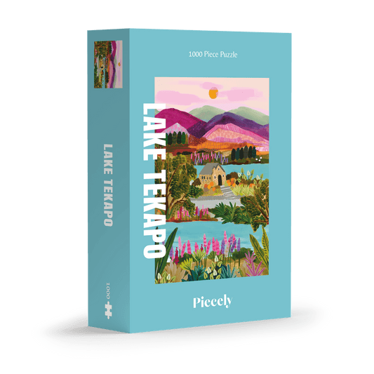 Abgebildet ist die Verpackung eines 1000-teiligen Puzzles mit dem Titel „Lake Tekapo“ der Marke Piecely. Die Schachtel ist in einem freundlichen, hellblauen Farbton gehalten. Im Zentrum befindet sich eine farbenfrohe Illustration einer Landschaft: Ein ruhiger See, umgeben von bunten Wildblumen, üppigem Grün und einem kleinen, detailreich gezeichneten Steinhaus mit Garten. Im Hintergrund erheben sich mehrfarbige Berge in Rosa-, Violett- und Grüntönen, darüber ein orangefarbener Sonnenuntergang vor einem rosa