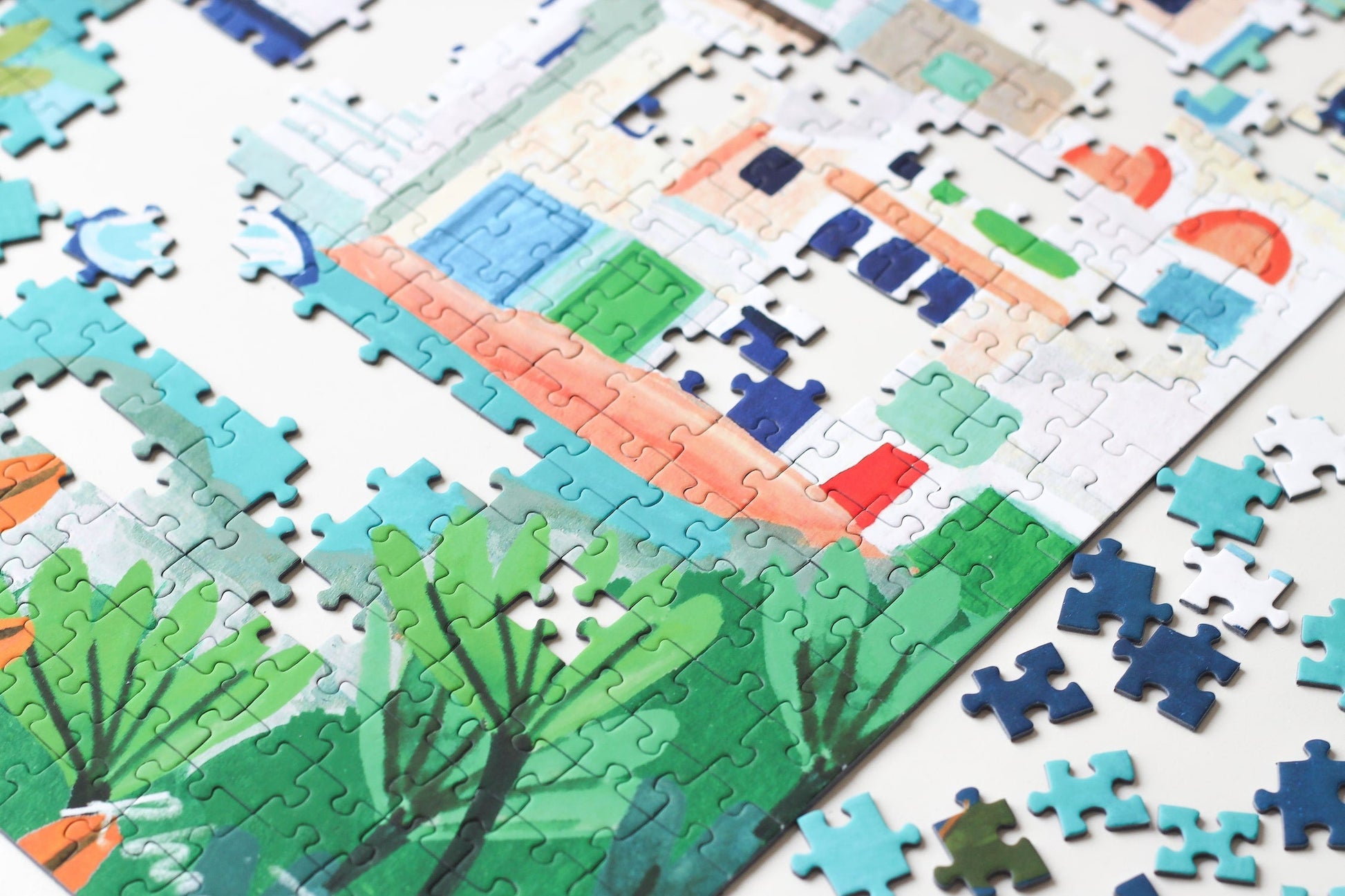 Außergewöhnliches 1000-Teile-Puzzle für Erwachsene, das einen Teil der griechischen Insel Milos zeigt. Zu sehen sind weiße Häuser and der Küste, Orangenbäume und Schiffe und Boote auf dem Meer.