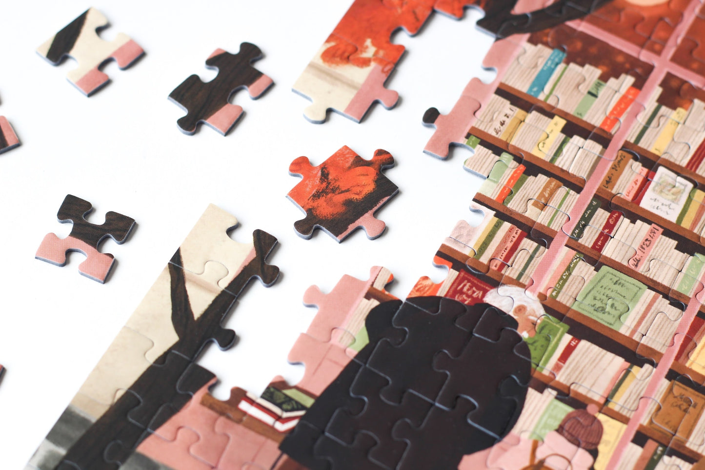 500-Teile-Puzzle „La Librairie“ von Piecely – Illustration einer herbstlichen Pariser Straßenszene vor einer kleinen Buchhandlung, auf rosa-brauner Verpackung.