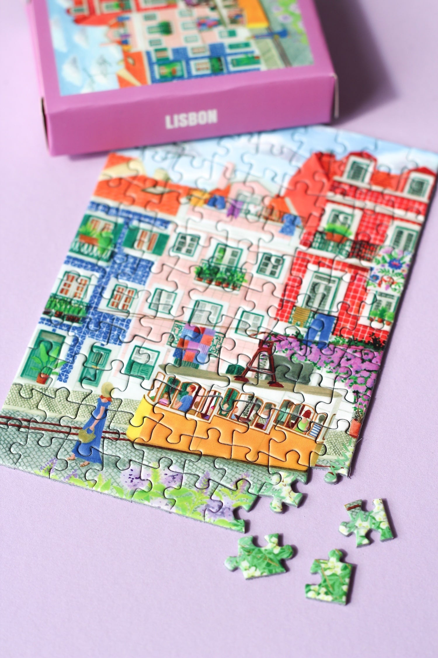 99-Teile-Mini-Puzzle „Lisbon“ von Piecely – Illustration einer farbenfrohen Straßenszene in Lissabon mit gelber Straßenbahn, auf pinker Verpackung.