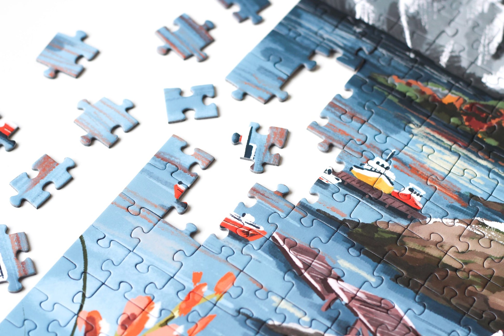 1000-Teile-Puzzle „Lofoten Norway“ von Piecely – Illustration einer norwegischen Küstenlandschaft mit schneebedeckten Bergen, roten Holzhäusern und Meer, auf olivgrüner Verpackung.