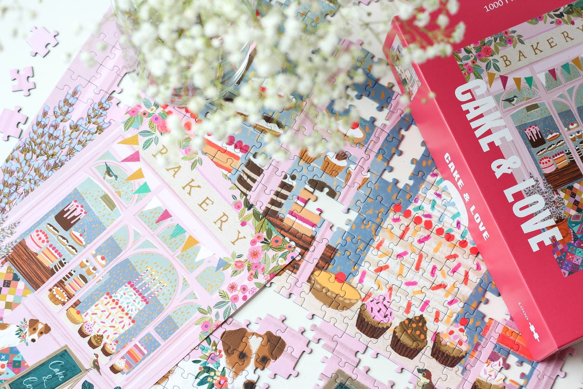 Außergewöhnliches 1000-Teile-Puzzle für Erwachsene, das eine rosa Bäckerei mit Torten, Kuchen und Cupcakes im Schaufenster und einen kleinen Hund für der Tür zeigt.