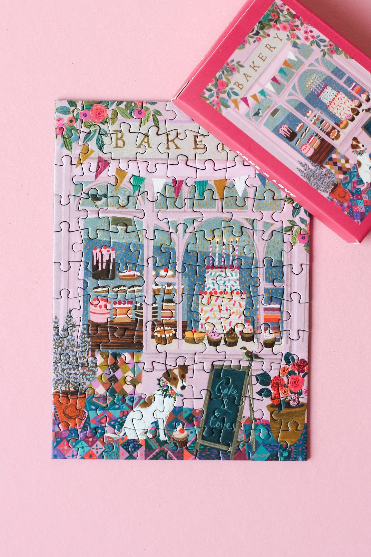 Plastikfreies Minipuzzle für Erwachsene, das eine rosa Bäckerei mit Torten und Cupcakes im Schaufenster und einen Hund vor der Tür zeigt.
