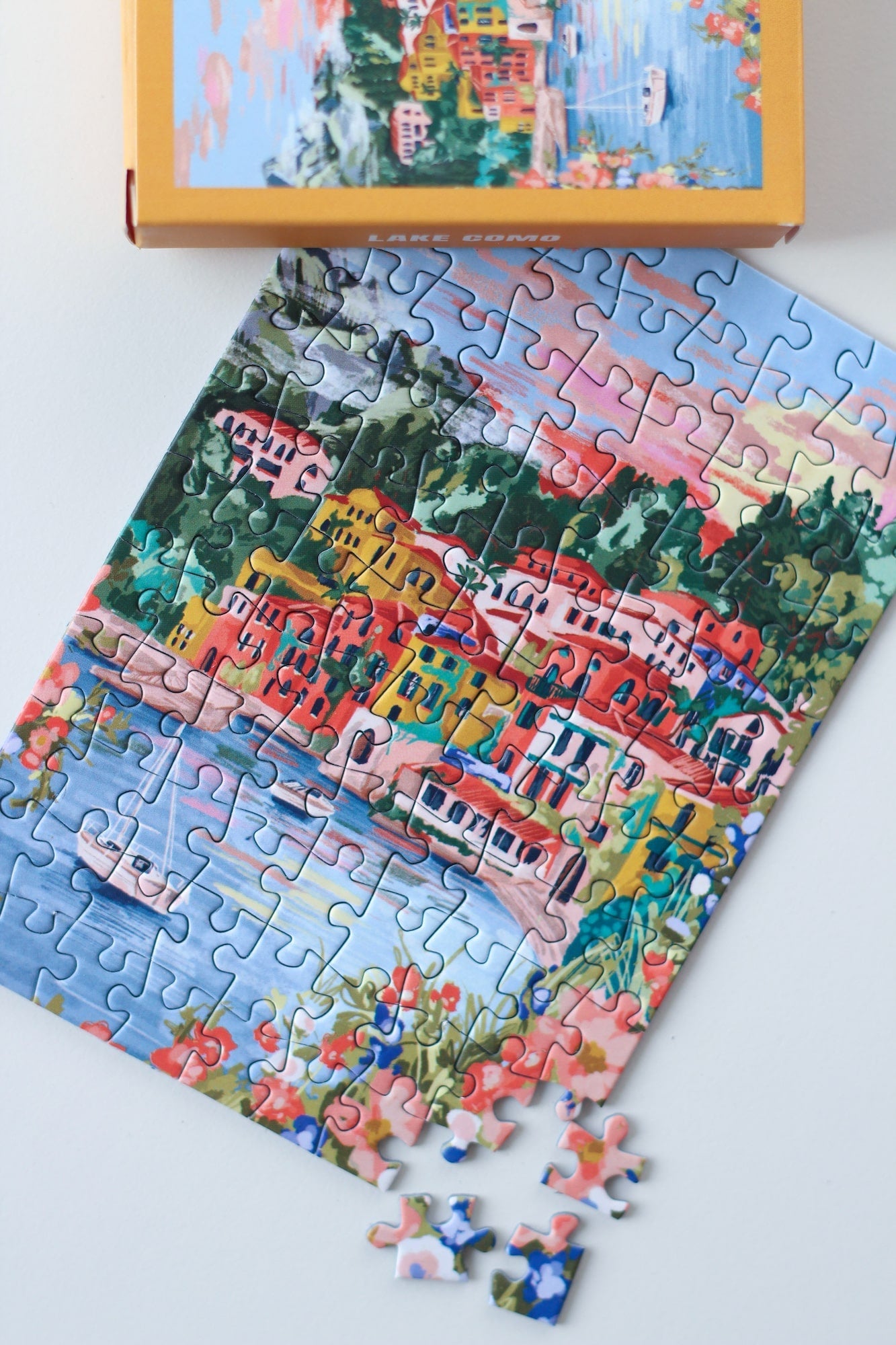 99-teiliges Minipuzzle für Erwachsene, das den Comer See in Varenna zeigt. In der Bucht befinden sich zwei Boote und die Sicht auf den See ist gesäumt von bunten Häusern.