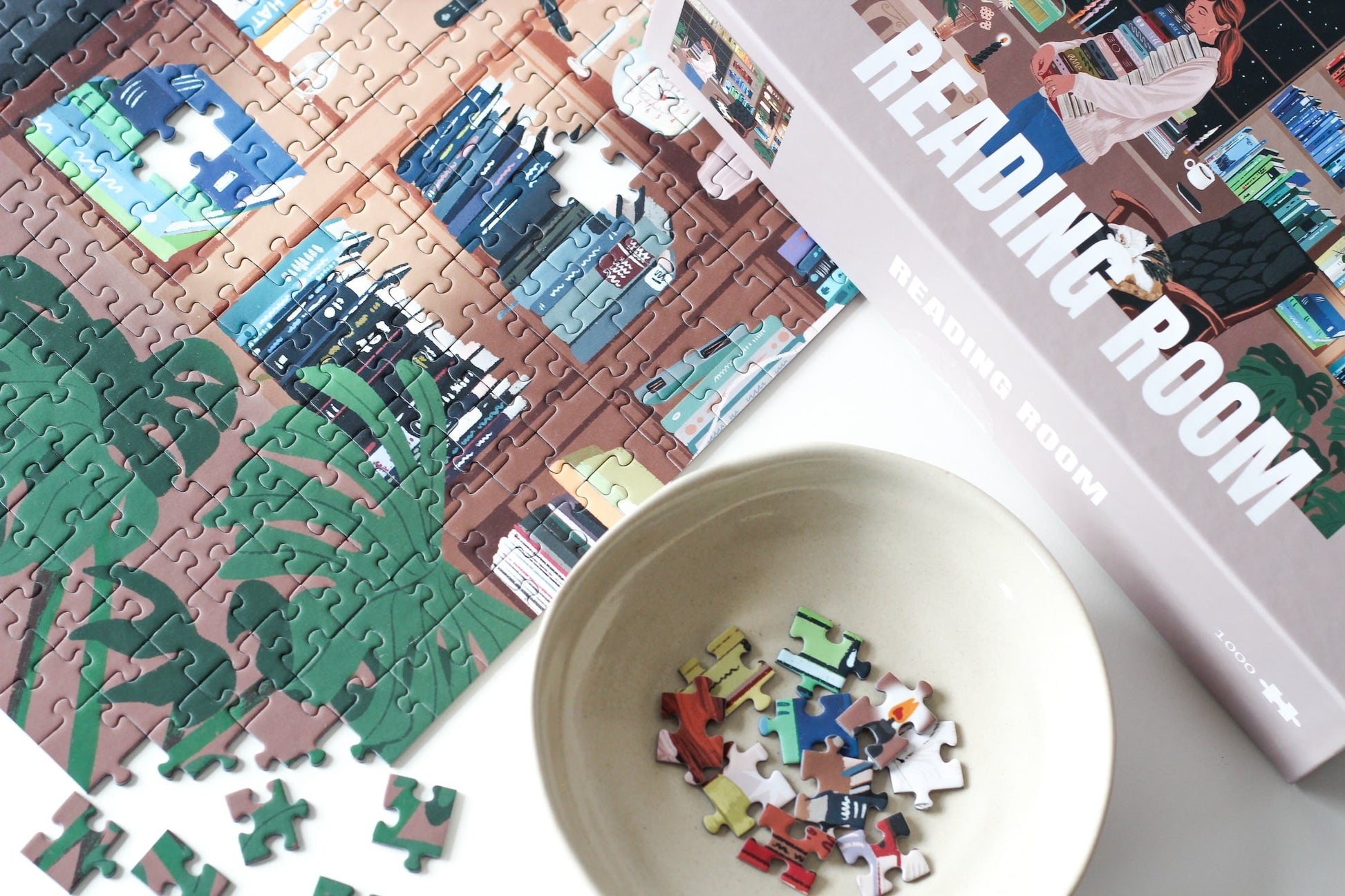 Nachhaltiges 1000-Teile-Puzzle, das eine Frau mit einem Stapel Bücher in der Hand zeigt. Im Hintergrund ist ein prall gefülltes Bücherregal und zwei süße Katzen.
