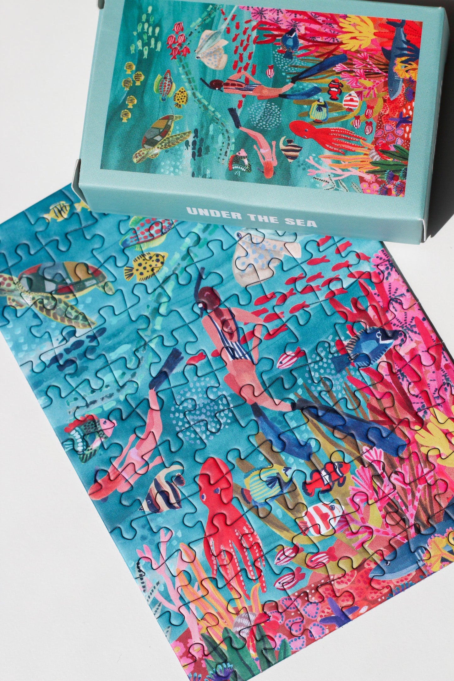 99-teiliges Under The Sea Minipuzzle für Erwachsene, das zwei Frauen beim Schnorcheln im Meer zeigt. Die Frauen sind umgeben von bunten Fischen, einem Oktopus, einem Rochen, einer Schildkröte und einem Hai. 