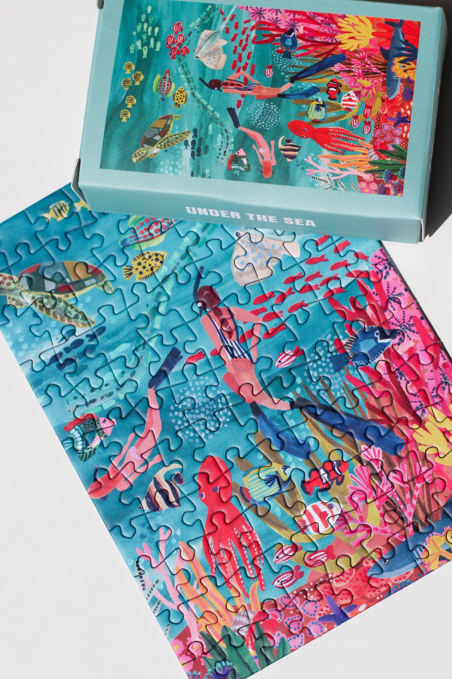 99-teiliges Under The Sea Minipuzzle für Erwachsene, das zwei Frauen beim Schnorcheln im Meer zeigt. Die Frauen sind umgeben von bunten Fischen, einem Oktopus, einem Rochen, einer Schildkröte und einem Hai. 